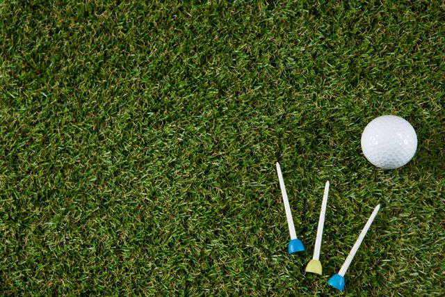 This image showcases a close-up view of a golf ball and colorful tees on a well-manicured grassy field, making it ideal for sports-related content, golfing tutorials, leisure and recreation promotions, or use in advertisements for golfing equipment.