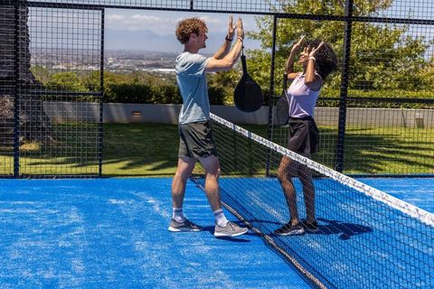Mixed-race partners high-fiving on blue padel court celebrating match win outdoors