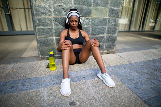 Focused fit african american woman wearing headphones, resting in street. healthy active lifestyle and outdoor fitness.