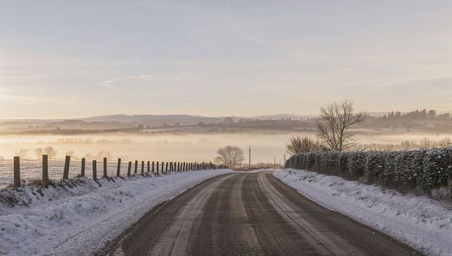 Curving snow-lined country road winding into misty winter valley at sunrise glow