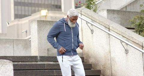Mature african american man walking down urban concrete stairs wearing hoodie and sweatpants