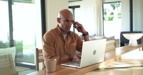 Mature professional working remotely at home kitchen island, making phone call and typing
