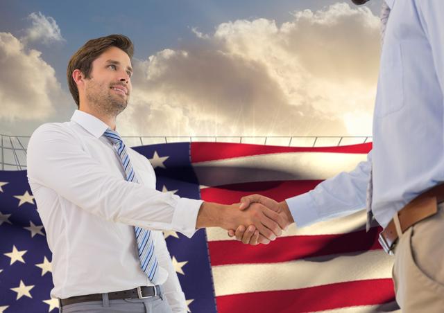 Businessmen are shaking hands outdoors against a backdrop of the American flag and a cloudy sky, symbolizing partnership, agreement, and patriotism. This can be used for representing business deals, national collaborations, and corporate success. Suitable for articles, brochures, websites, and presentations emphasizing business and patriotism.