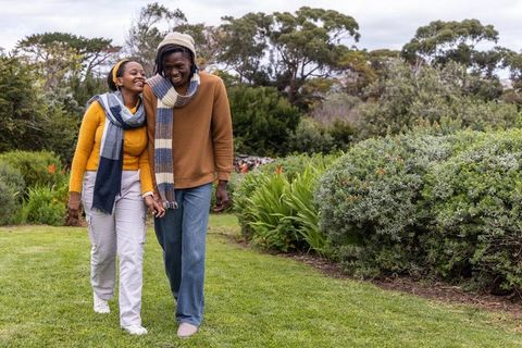 African american couple walking hand-in-hand through park wearing sweaters and scarves