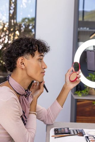 Stylish man applying makeup under ring light
