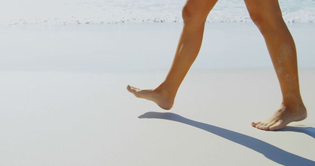 Barefoot legs of a person are captured mid-stride on a sandy beach, with copy space. The image evokes a sense of relaxation and freedom associated with beach vacations or leisurely walks by the sea.
