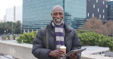 Senior african american professional smiling holding coffee and tablet on urban terrace
