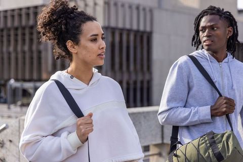 Young woman and man walking and talking on urban rooftop carrying backpack and duffel bag