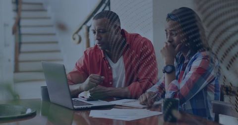 Couple reviewing finances and planning budget at home desk using laptop and documents