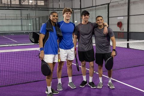 Padel doubles team posing on purple indoor court celebrating teamwork and camaraderie