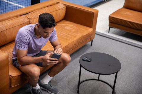 African american man checking phone while resting on tan leather sofa in courtside lounge
