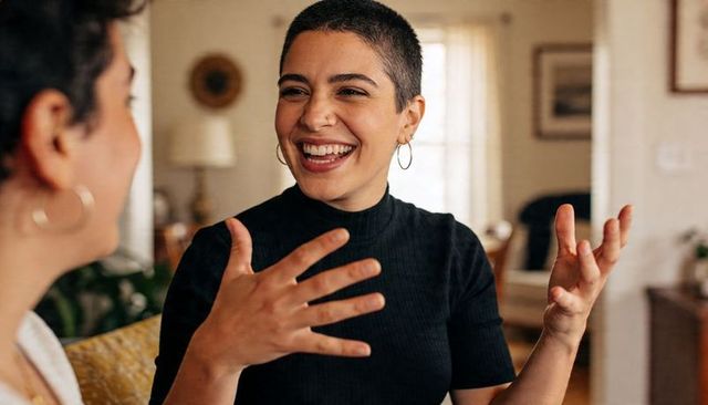 Smiling buzzcut woman gesturing while chatting in cozy living room with hoop earrings