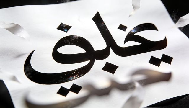Gleaming arabic calligraphy on white paper with silver ribbons and glitter macro closeup