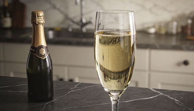 Champagne flute on dark marble countertop, bubbles rising, foil glinting, luxury kitchen