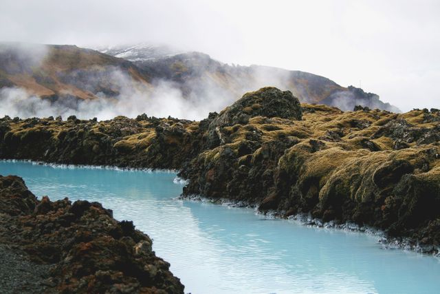 Image shows a peaceful geothermal pool with turquoise water surrounded by rocky terrain and moss-covered rocks in an Icelandic landscape. Mist rises in the background, creating a tranquil and atmospheric scene. Ideal for travel blogs, nature magazines, or tourism promotions featuring Iceland's unique natural features.