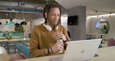 African american man working in modern coworking lounge holding reusable bottle wearing headphones