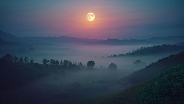 Full moon over misty hills creates serene nighttime landscape