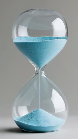 Vertical video of blue sand flowing through clear glass hourglass on neutral studio table