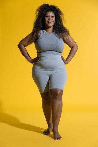 Smiling plus-size african american woman posing in grey activewear on vibrant yellow