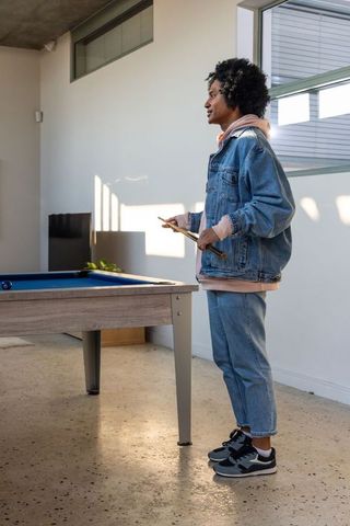 African american man standing by pool table holding cues in modern minimalist rec room
