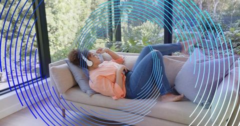 Woman listening to music relaxing on sofa with headphones in sunlit modern living room