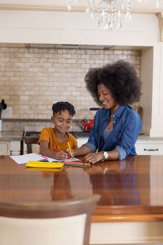 African american mother helping son with homework at kitchen island using colored pencils
