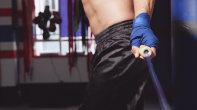 Focused on a male boxer jumping rope in a boxing gym. Punchbags are visible in the background. Can be used for fitness training programs, athletic advertisements, sports promotions, and articles on boxing techniques and workouts.