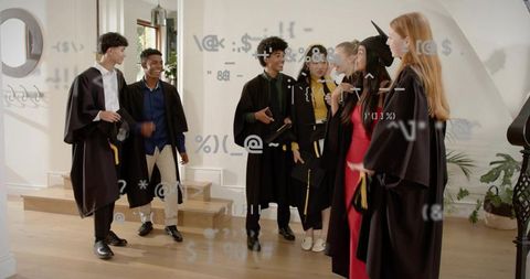Graduates chatting in foyer wearing caps and gowns holding diplomas and mortarboards