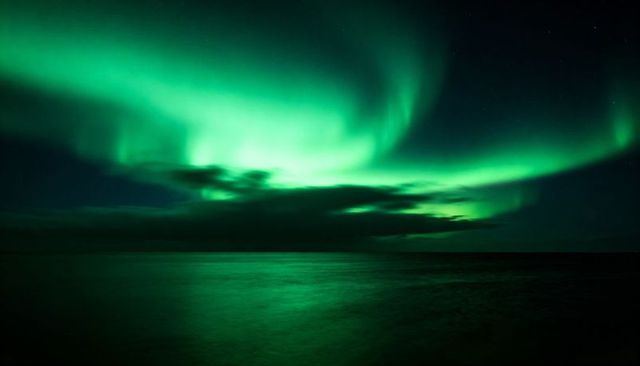 Aurora borealis dancing over calm sea, green curtains reflecting on tranquil night water