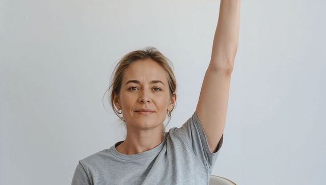 Confident middle-aged woman raising hand in minimal studio portrait wearing grey tee