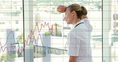 Gazing clinician shading eyes while viewing healthcare analytics on hospital glass wall