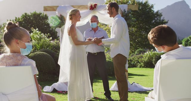 Caucasian bride groom and wedding officiant wearing face mask standing at outdoor altar. romantic summer wedding outdoors during coronavirus covid 19 pandemic.