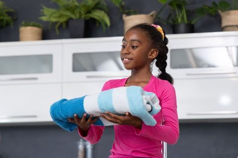 African american girl holding rolled beach towel in modern kitchen, home chore concept