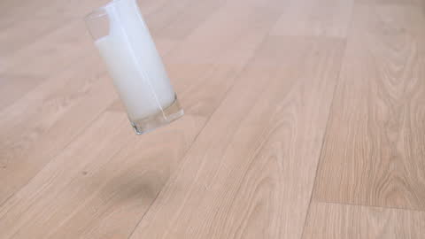 Glass of Milk Splashing on Wooden Floor in Slow Motion