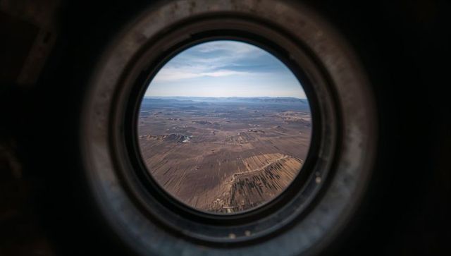 Aircraft Porthole Framing Aerial Desert Furrows and Distant Mountains