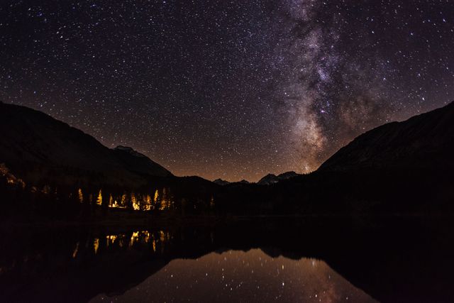 Overlooking a tranquil mountain lake, the Milky Way and numerous stars fill the night sky, reflected in the still water below. This serene outdoor setting evokes feelings of wonder and peace, ideal for nature-themed projects, travel advertisements, or astronomy content. Perfect for use in calendars, wallpapers, and educational materials about the universe.
