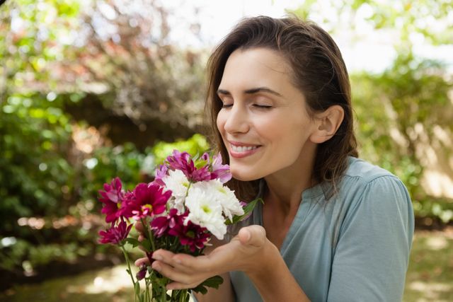 This image captures a woman smiling and enjoying the scent of fresh flowers in a garden. Ideal for use in lifestyle blogs, gardening websites, wellness and relaxation promotions, and advertisements for floral products. It conveys a sense of peace, happiness, and connection with nature.