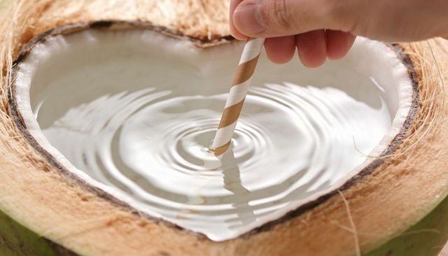 Hand stirring striped paper straw in heart-shaped coconut, water ripples closeup, natural