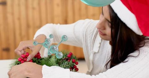 Woman wearing santa hat crafting festive wreath with red berries and blue ornament