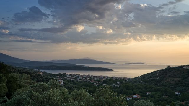 Mediterranean hillside village with lush greenery and sea view during sunset. Peaceful coastal atmosphere with calm waters and scenic beauty, suitable for travel brochures, nature photography collections, and tourism promotions.