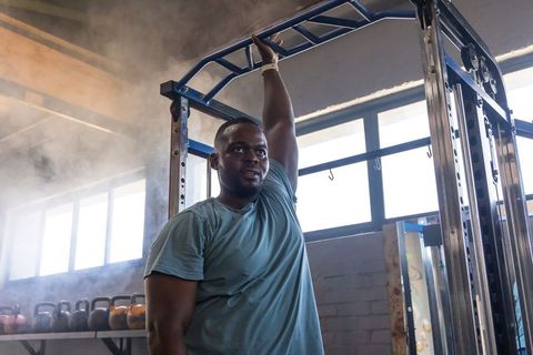 African man holding pull-up bar, resting between sets in industrial gym with kettlebells