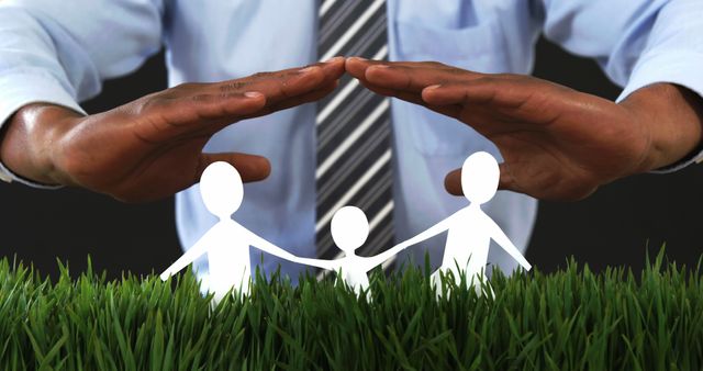African American hands form a protective roof over a paper cutout of a family on a grassy surface, symbolizing insurance or security, with copy space. It represents the concept of safeguarding family and home, with a focus on the importance of protection and care.