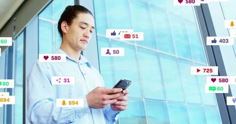 Japanese businessman holding smartphone by glass wall with social media notifications