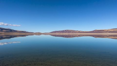 Mirrorlike alpine lake reflecting clear sky and distant hills on high plateau