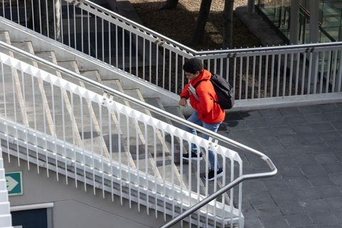 Teen climbing urban concrete stairs wearing red hoodie carrying backpack adjusting strap