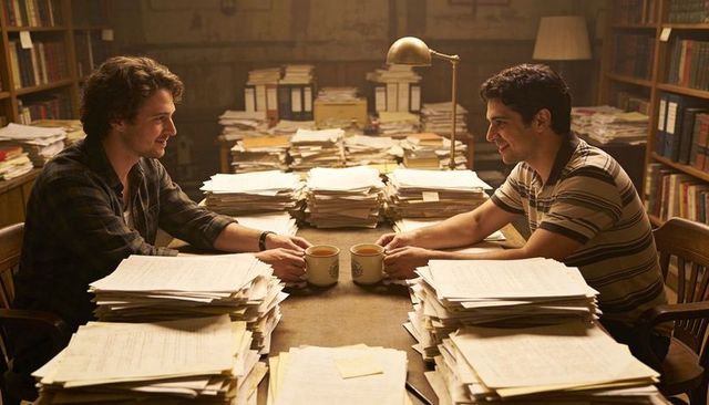 Two researchers poring over archival paperwork in library sharing coffee and conversation