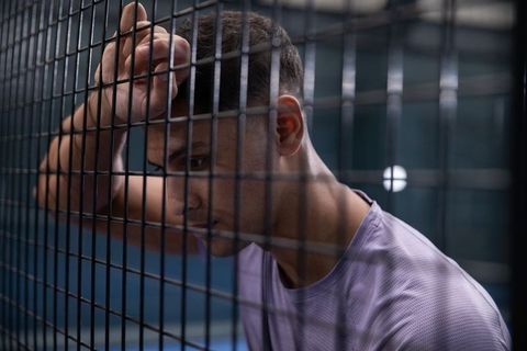Exhausted Athlete Leaning on Mesh Fence After Intense Training Showing Contemplation