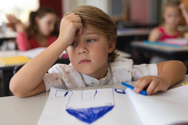 Front view of sad schoolboy studying in classroom sitting at desks in school