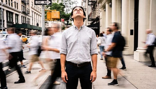 Young professional standing still amid hustle of busy city street looking up
