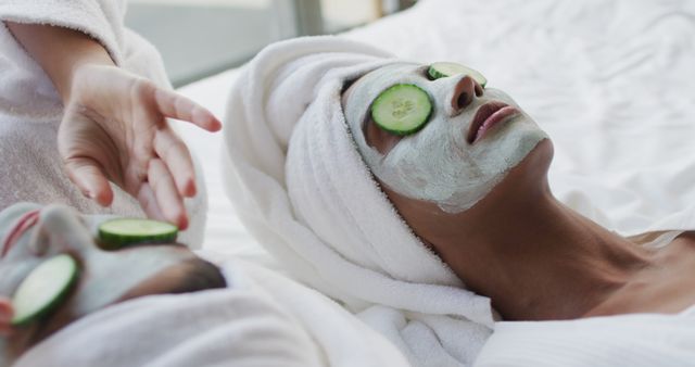 Women are lying down with cucumbers on their eyes and wearing facemasks, towels wrapped around their heads. This image is ideal for usage in wellness or beauty industry marketing, spa brochures, skincare product advertisements, pampering and self-care guide illustrations, and health and relaxation blogs.